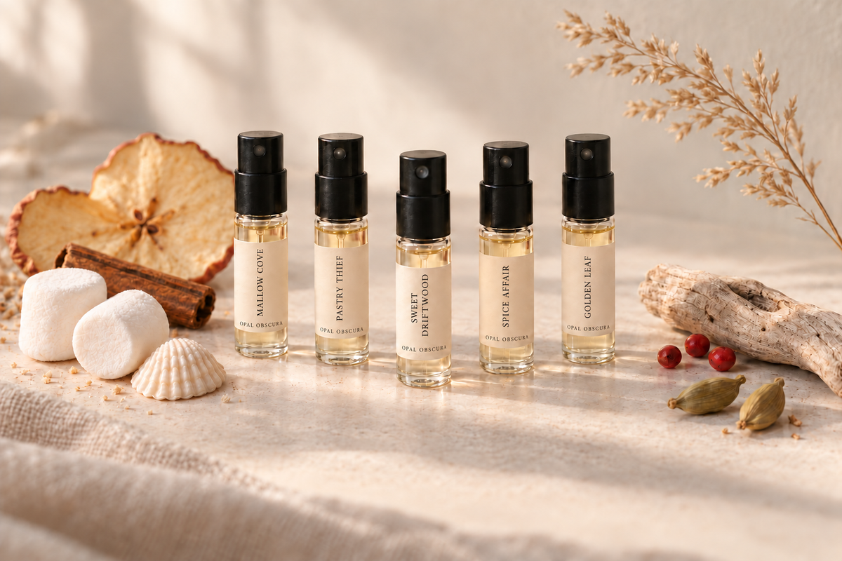 The Fall & Winter Fragrance Flight: five 2 mL extrait samples (Pastry Thief, Milk Drunk Rice, Sweet Driftwood, Spice Affair and Golden Leaf) on linen with dried apple, cinnamon, driftwood, pink peppercorns and cardamom
