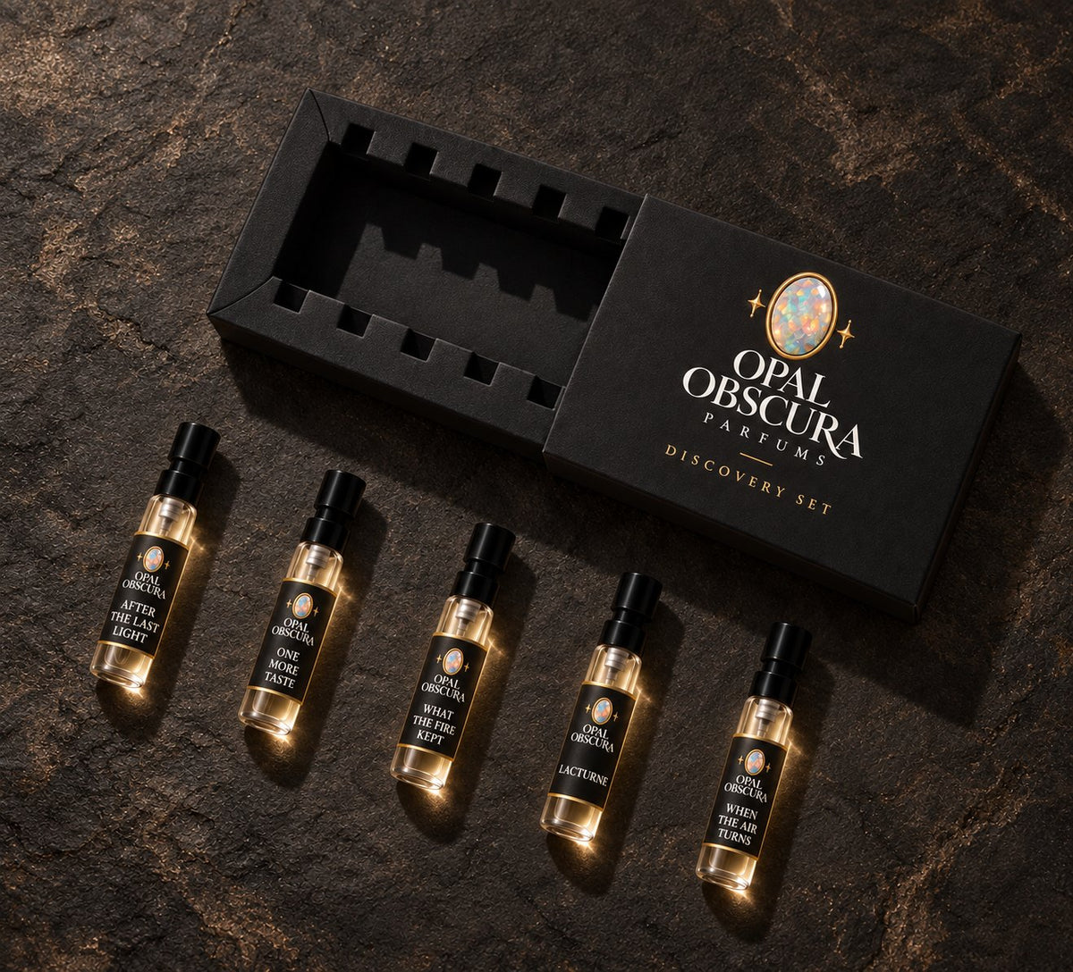Opal Obscura Fall Discovery Set: five 2 mL sprays of After the Last Light, One More Taste, What the Fire Kept, Lacturne, and When the Air Turns beside a black presentation box on charcoal stone.